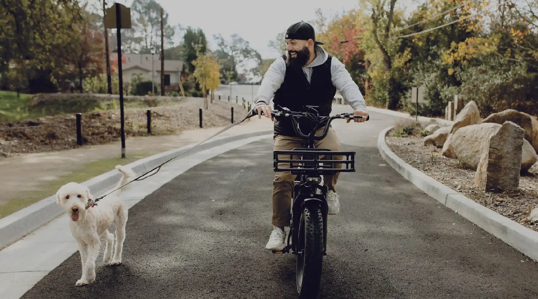 Electric cargo bike with a front basket being ridden alongside a white dog.