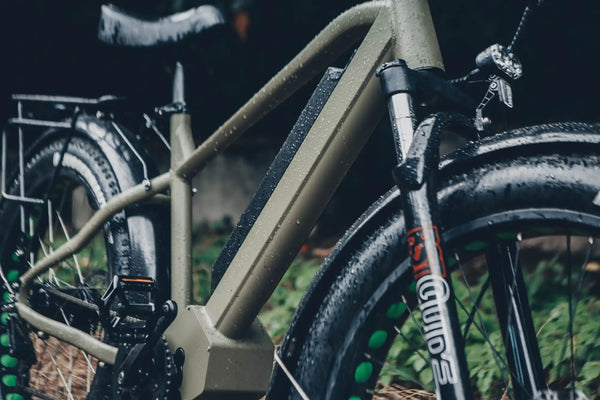 Tan-colored electric bicycle with front suspension forks and fenders.